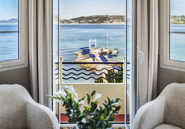 A room with a view of a dock and boats, a balcony with a railing, and a plant in the foreground. - Hotel Belles Rives (Antibes)
