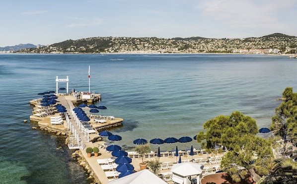 A waterfront hotel with a pier, lounge chairs, and umbrellas. - Hotel Belles Rives (Antibes)