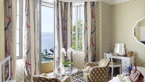 A hotel room with a checkered floor, a desk, a chair, a bed, and a view of the sea. - Hotel Belles Rives (Antibes)