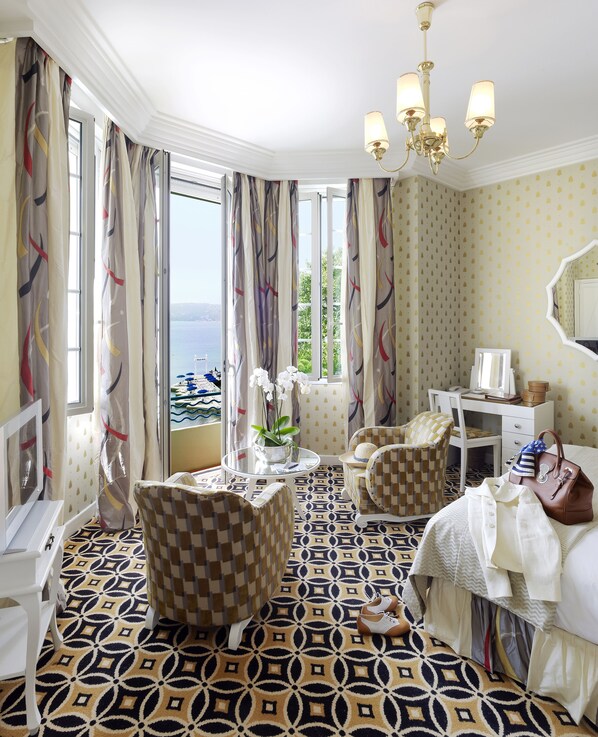 Une chambre d’hôtel avec un sol à carreaux, un bureau, une chaise, un lit et une vue sur la mer.