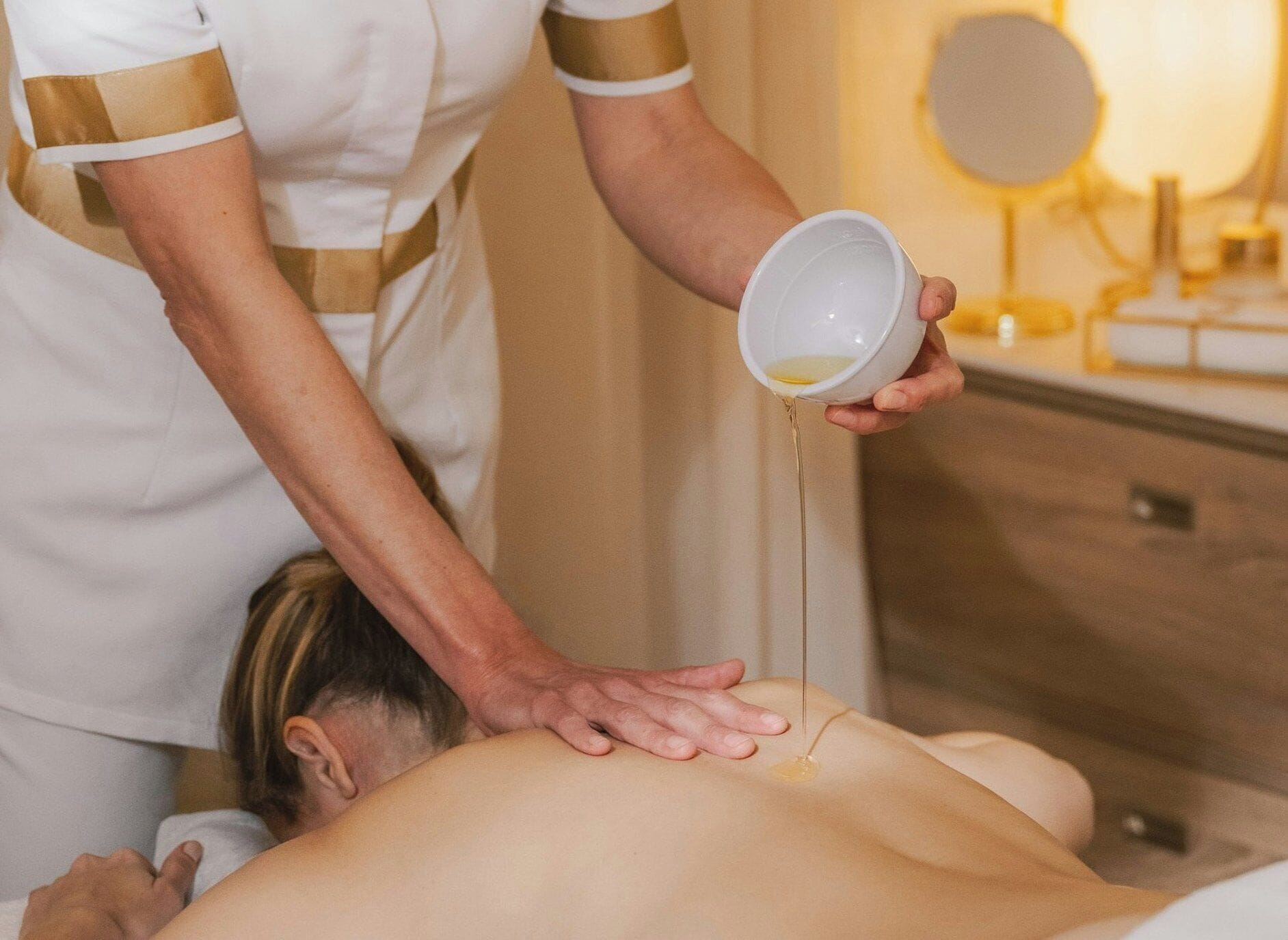 A person receiving a massage with a bowl of oil being poured on their back.
