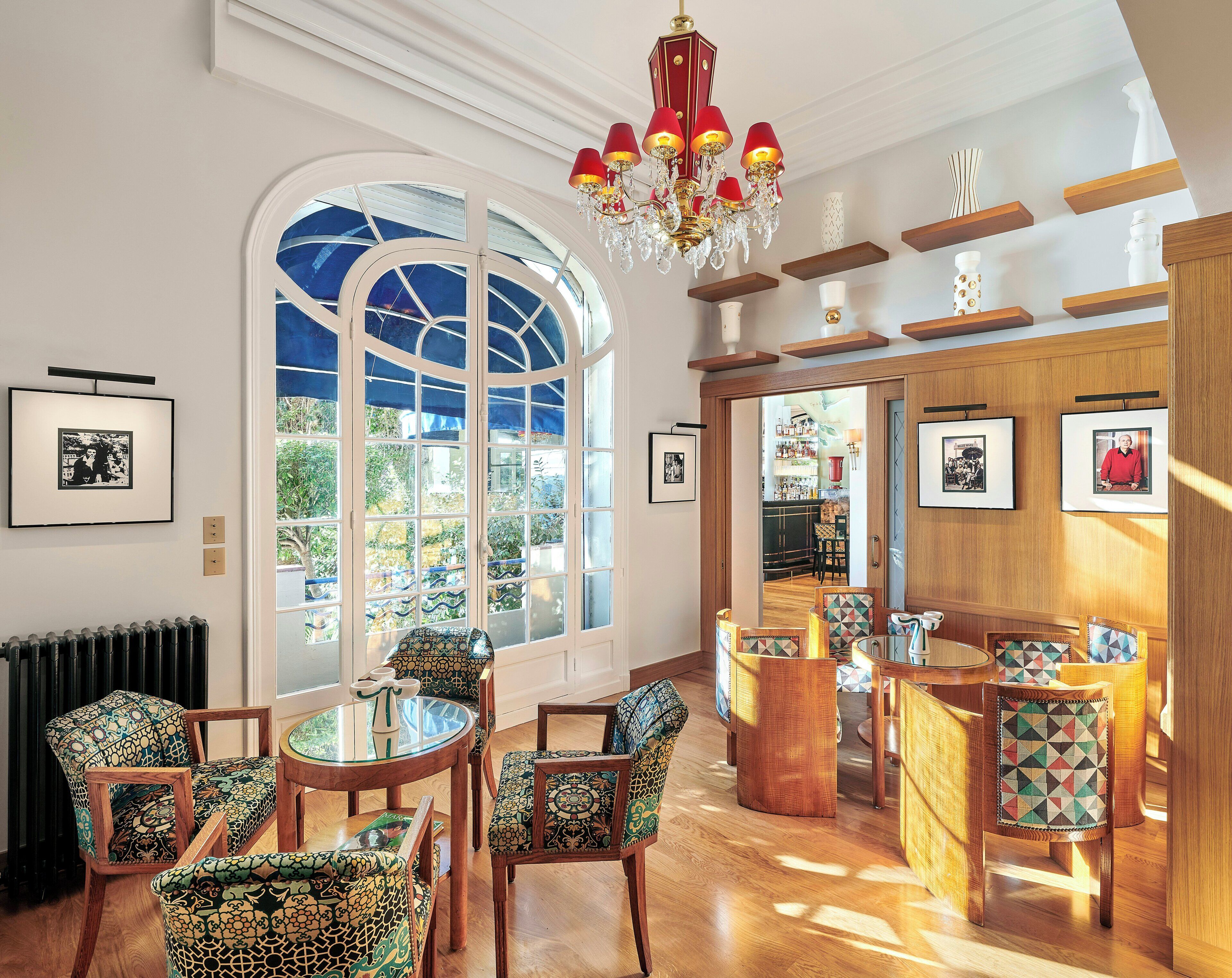 A room with a large arched window, a chandelier, and a bar area with chairs and tables.