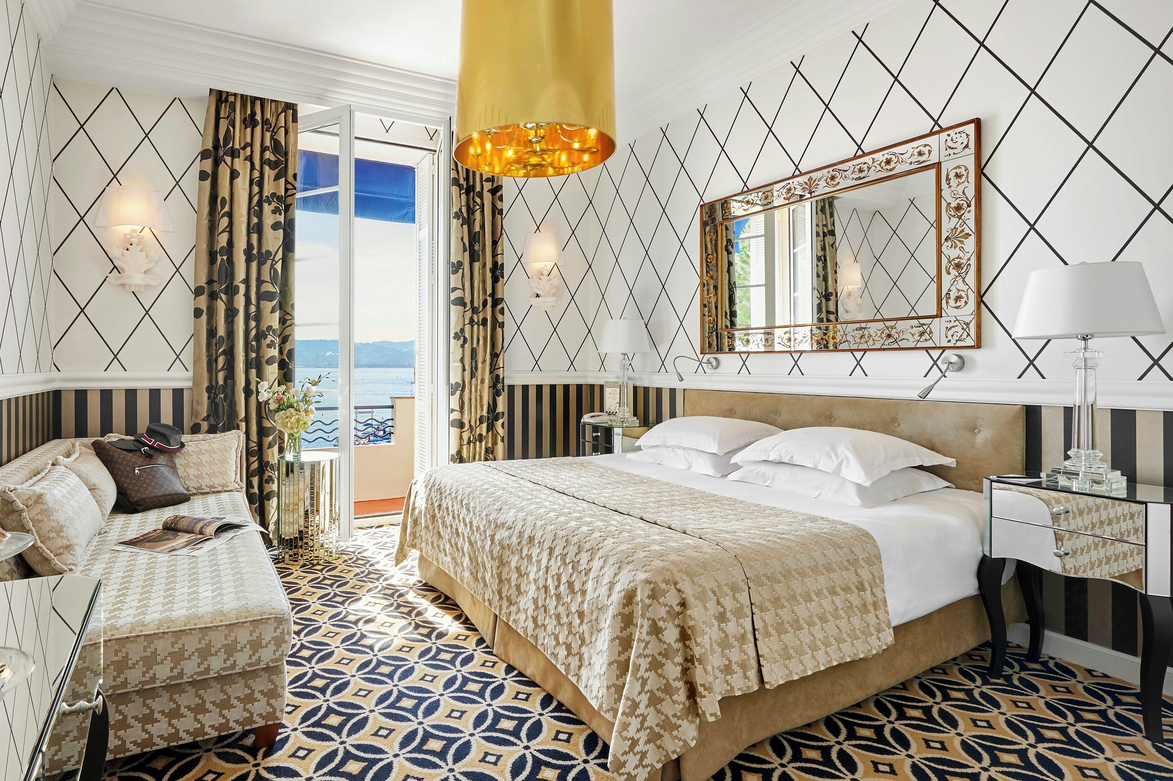 Une chambre d’hôtel avec un grand lit, un coin salon avec un fauteuil, une table de chevet et un miroir.