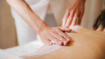 Et nærbillede af hænder, der giver en massage på en persons ryg.