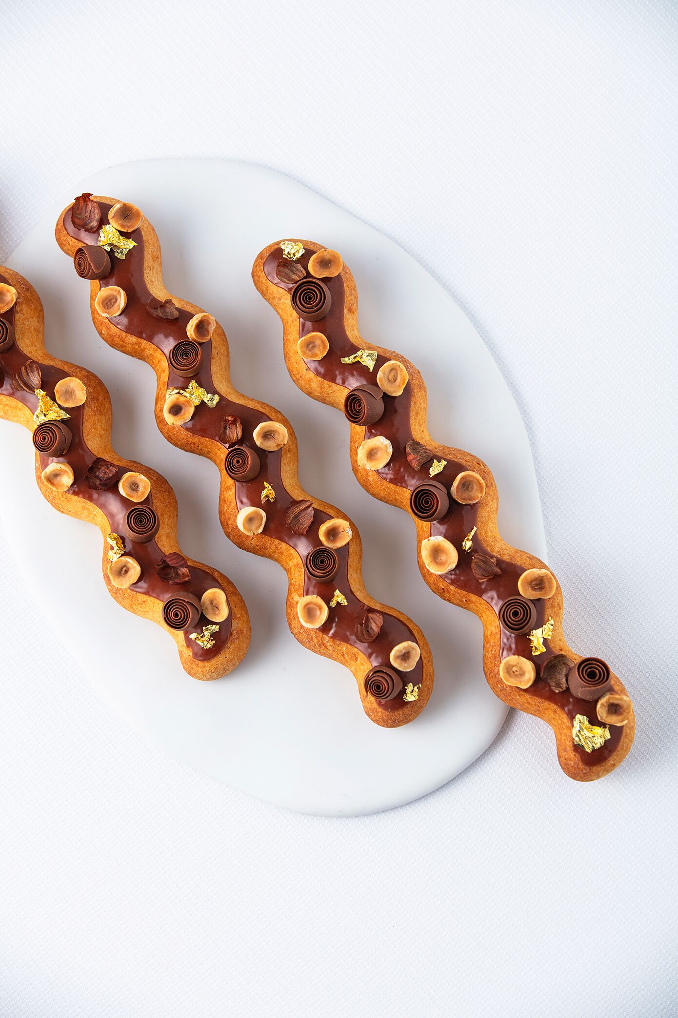 En wienerbrød dækket med chokolade, nødder og dekorative elementer på en hvid tallerken.