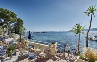 Une terrasse avec des sièges extérieurs, donnant sur une étendue d’eau où l’on peut voir des bateaux et, au loin, la terre ferme.