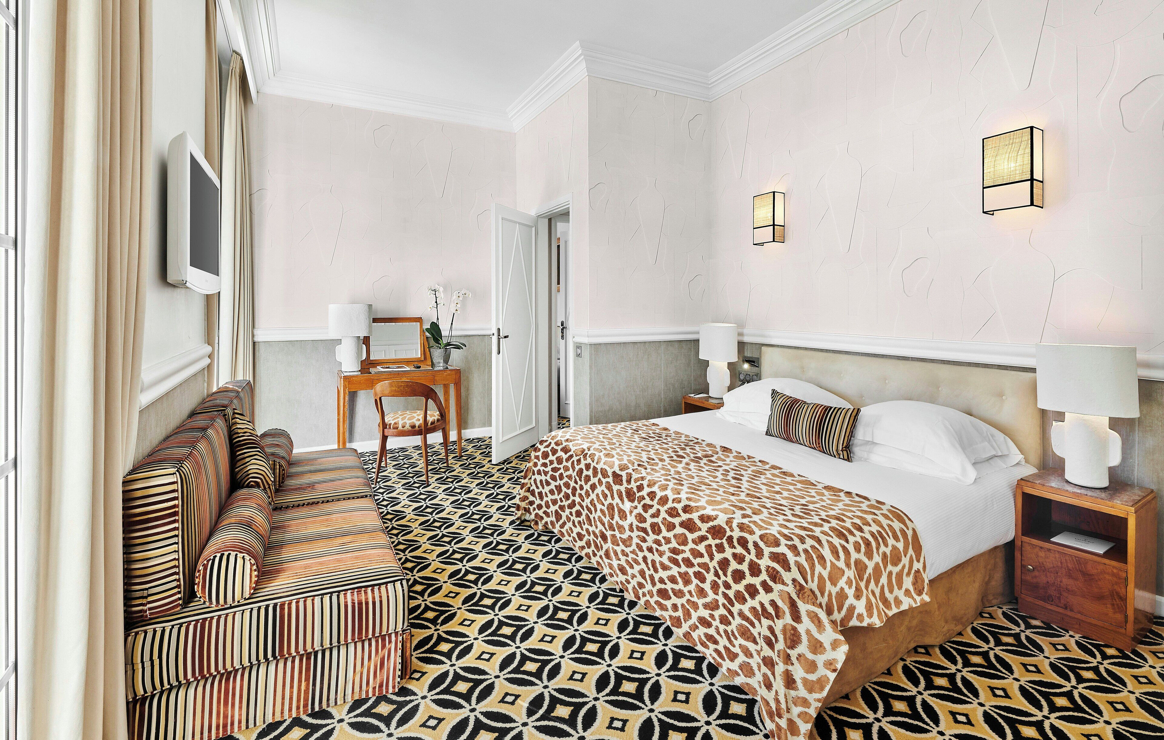 Una habitación de hotel con piso estampado, una cama con colcha de jirafa, un sofá a rayas y un escritorio con lámpara.