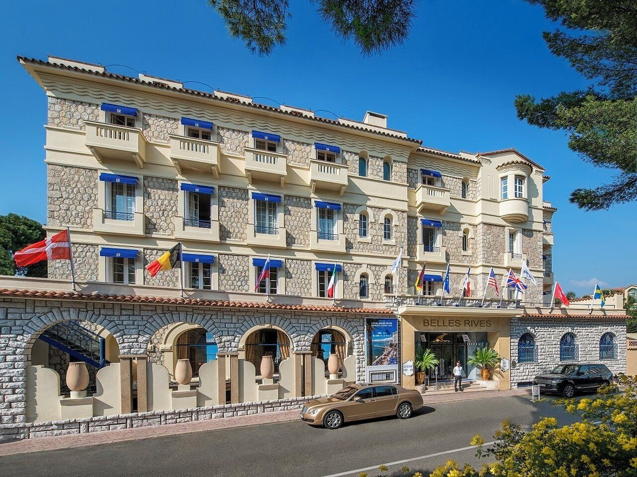 Un hotel de varios pisos con balcones, fachada de piedra y banderas.