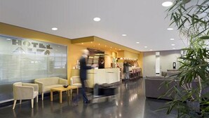 Un moderno vestíbulo de hotel con una recepción, zona de estar y un amplio ventanal donde se ve el nombre del hotel.