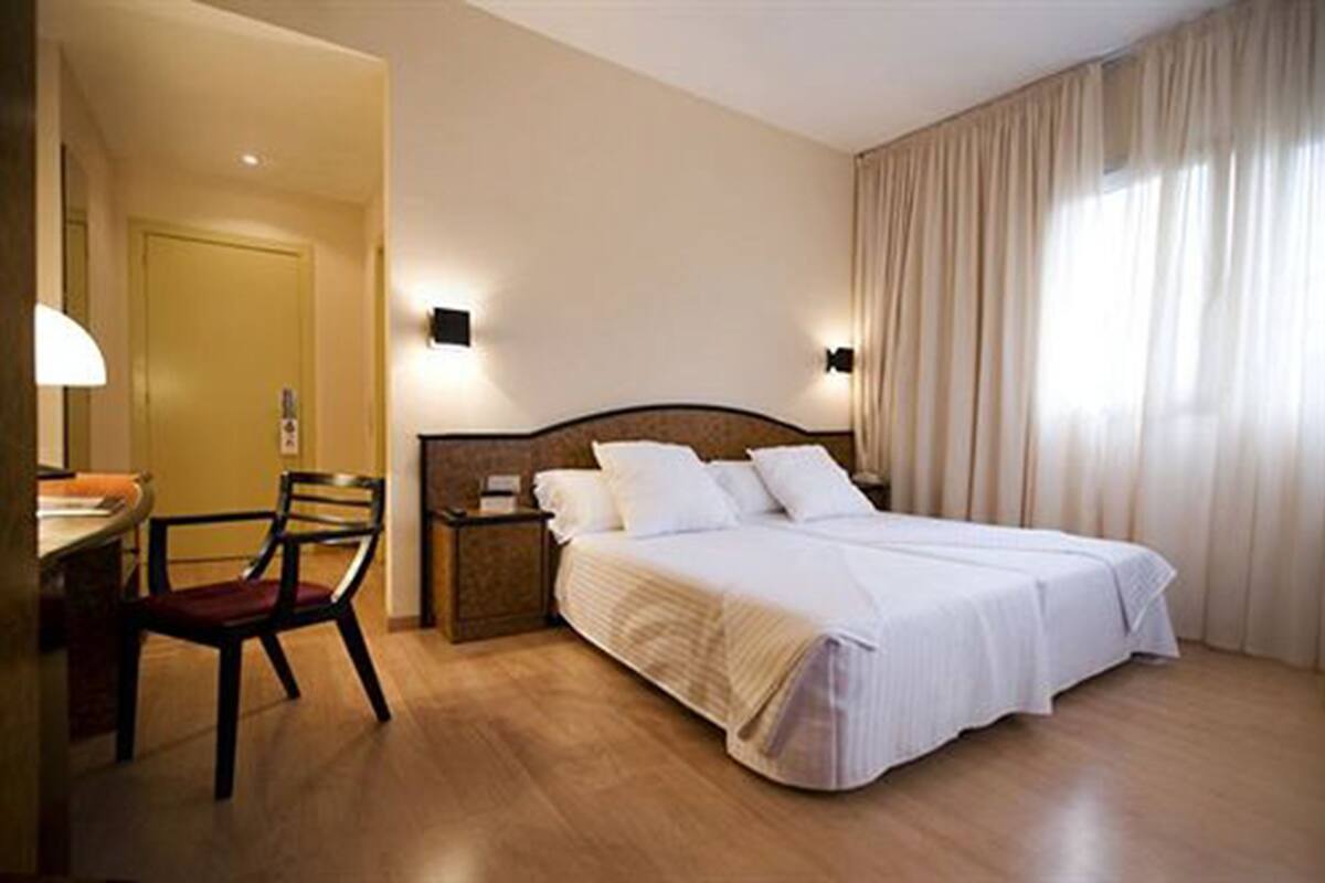 Una habitación de hotel con cama, escritorio, silla, mesita de noche y lámpara.