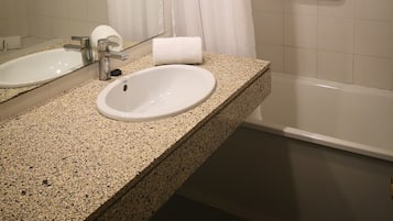 Un baño con encimera de granito, dos lavamanos, un espejo, cortina de ducha y barra de apoyo.