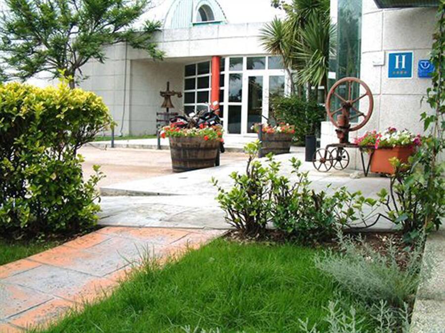 Entrada de hospital con rampa para sillas de ruedas, plantas en macetas y un timbre.