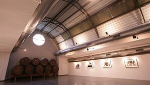 Una galería amplia con techo alto y tragaluces, que presenta varios barriles de madera y obras de arte enmarcadas en las paredes.