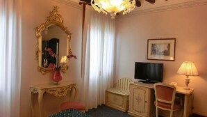A hotel room with a large ornate mirror, a television, a small cabinet, a chair, and a lamp. - Hotel Diana (Venice)