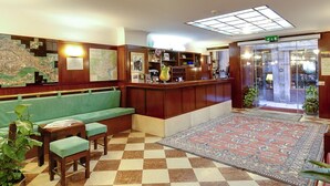 A lobby with a checkered floor, a green sofa, a reception desk, and a map on the wall. - Hotel Diana (Venice)