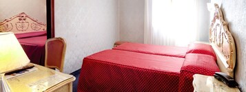 A hotel room with two beds, a desk with a lamp, a chair, and a telephone.
