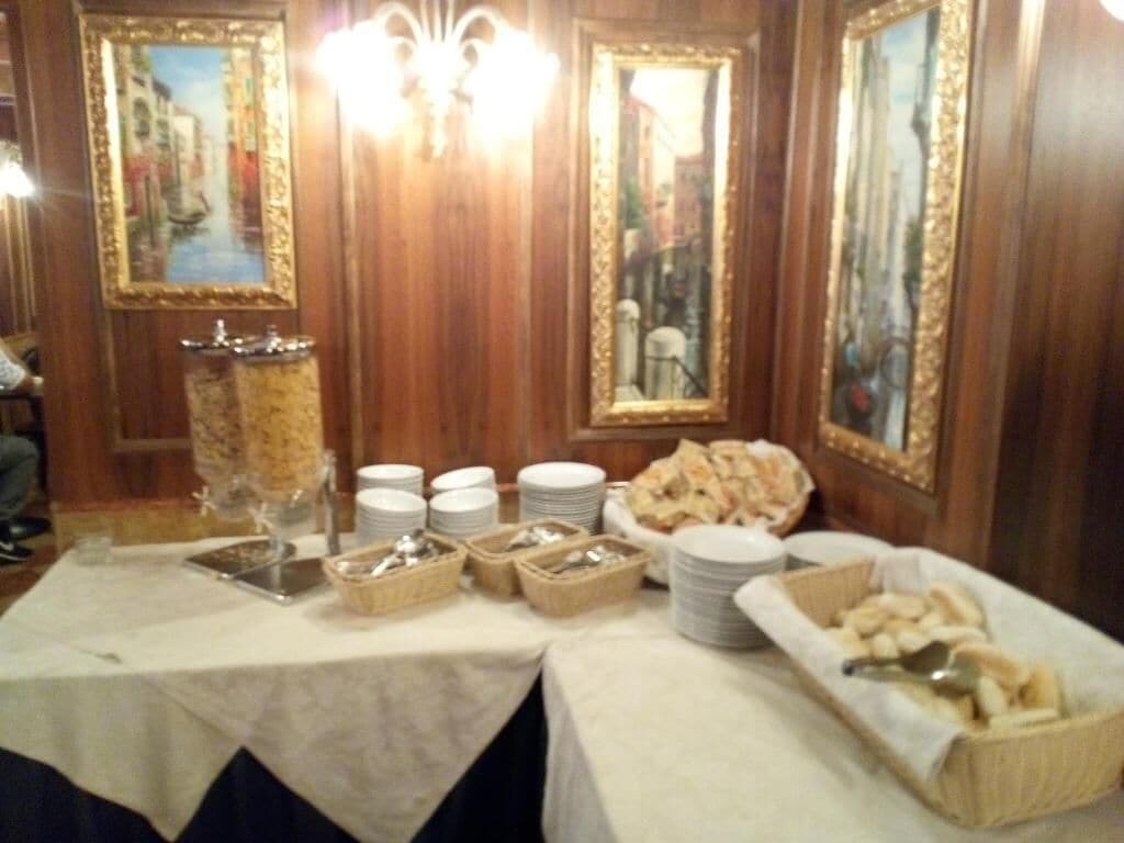 Une table de buffet garnie de divers plats et de différents plats de service, placée devant un mur en bois orné de tableaux encadrés.