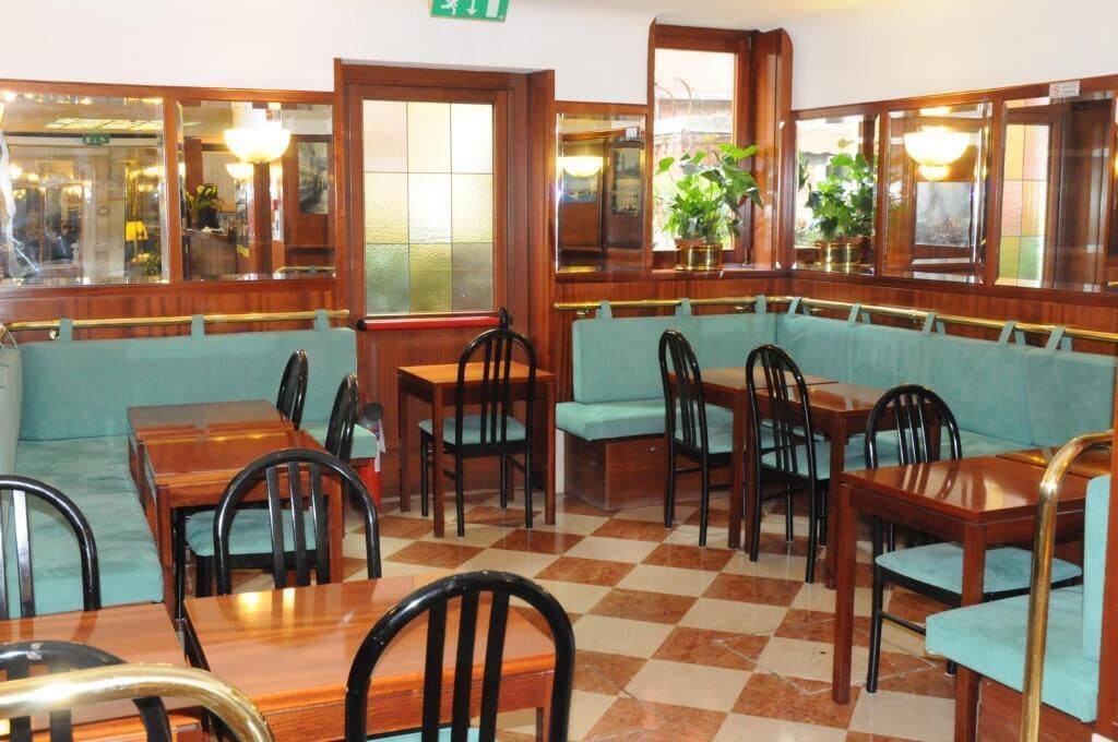 A restaurant with wooden tables and chairs, a checkered floor, and large windows with reflections.