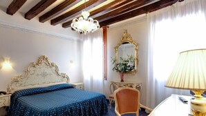 A hotel room with a bed, a desk, a chair, a lamp, a mirror, and a chandelier. - Hotel Diana (Venice)