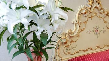 A vintage-style bedside table with a vase of white flowers, a decorative headboard, and a red patterned bedspread.