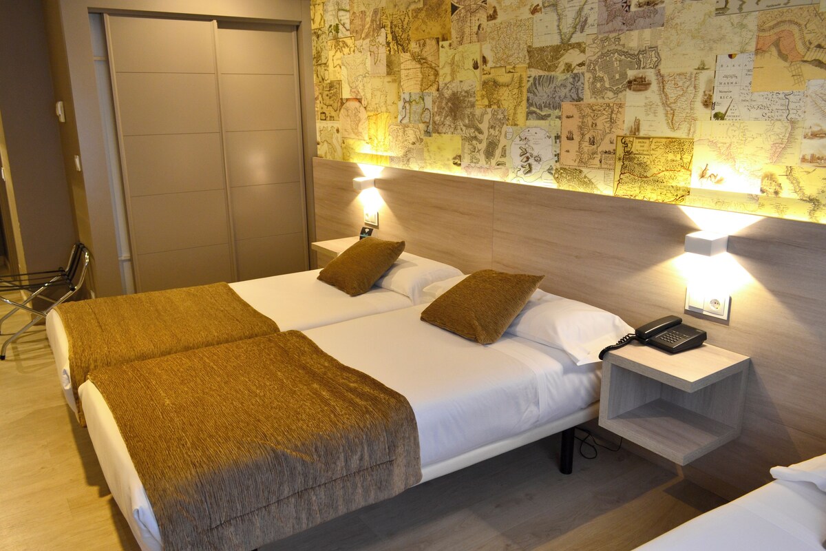 Ein Hotelzimmer mit zwei Betten, einem Nachttisch mit Telefon, einer Wandkarte und einer Tür zu einem Schrank.