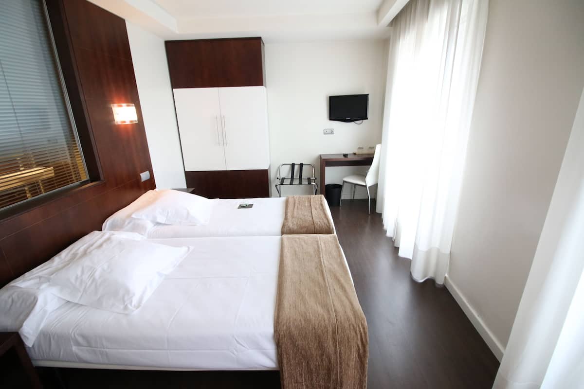 Habitación de hotel con dos camas, un escritorio, una silla, un televisor y una ventana con cortinas.