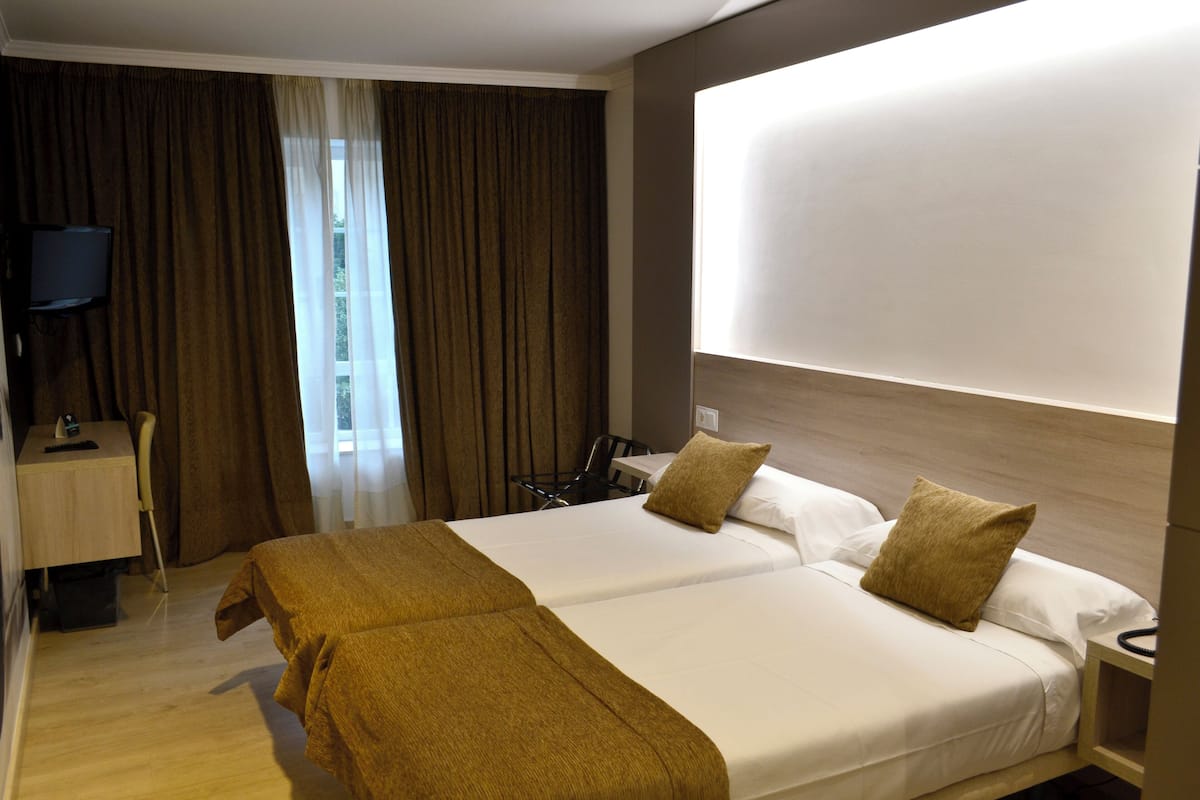 Habitación de hotel con una cama grande, un escritorio con silla, televisión y ventana con cortinas.
