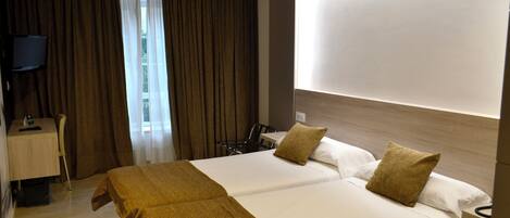 A hotel room with a large bed, a desk with a chair, a television, and a window with curtains.