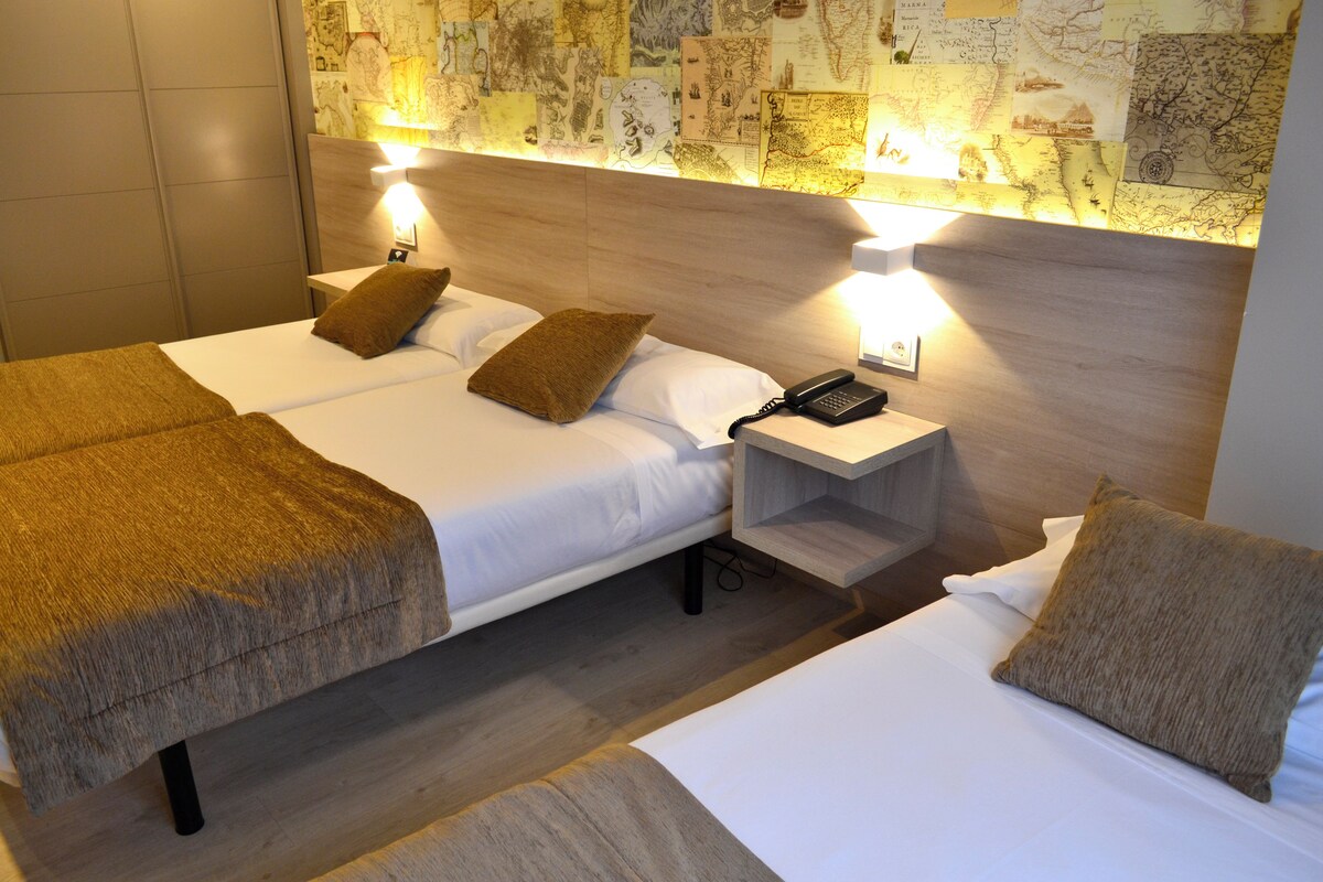 Une chambre d’hôtel avec deux lits, une table de chevet avec un téléphone et un mur décoré de cartes.