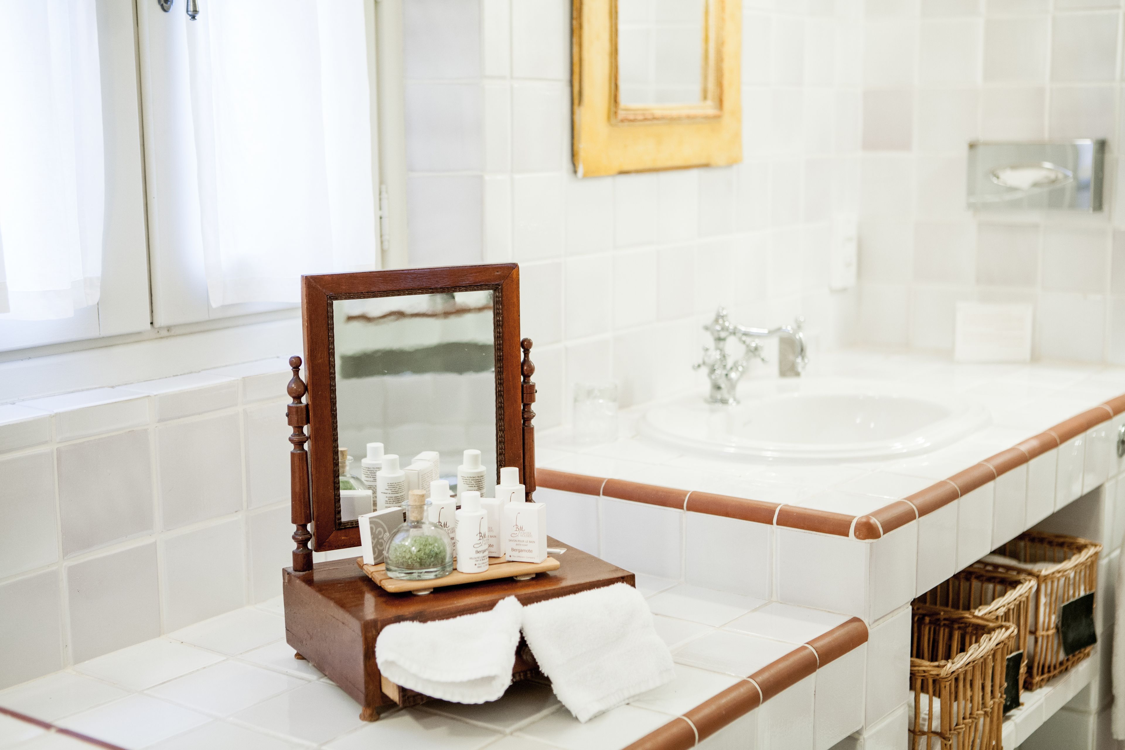 Une salle de bain avec un meuble-lavabo en bois, un grand miroir et un évier. On y trouve des articles de toilette sur le meuble-lavabo et une serviette sur le sol.