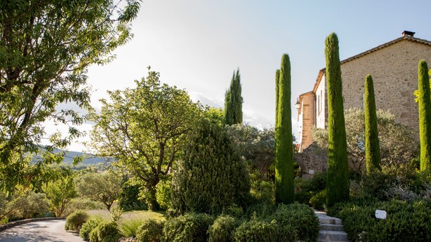 A garden with a stone building, tall cypress trees, and a winding path.