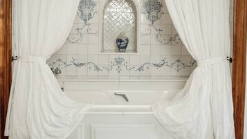 Un baño con bañera, cortinas blancas y un espejo decorativo.