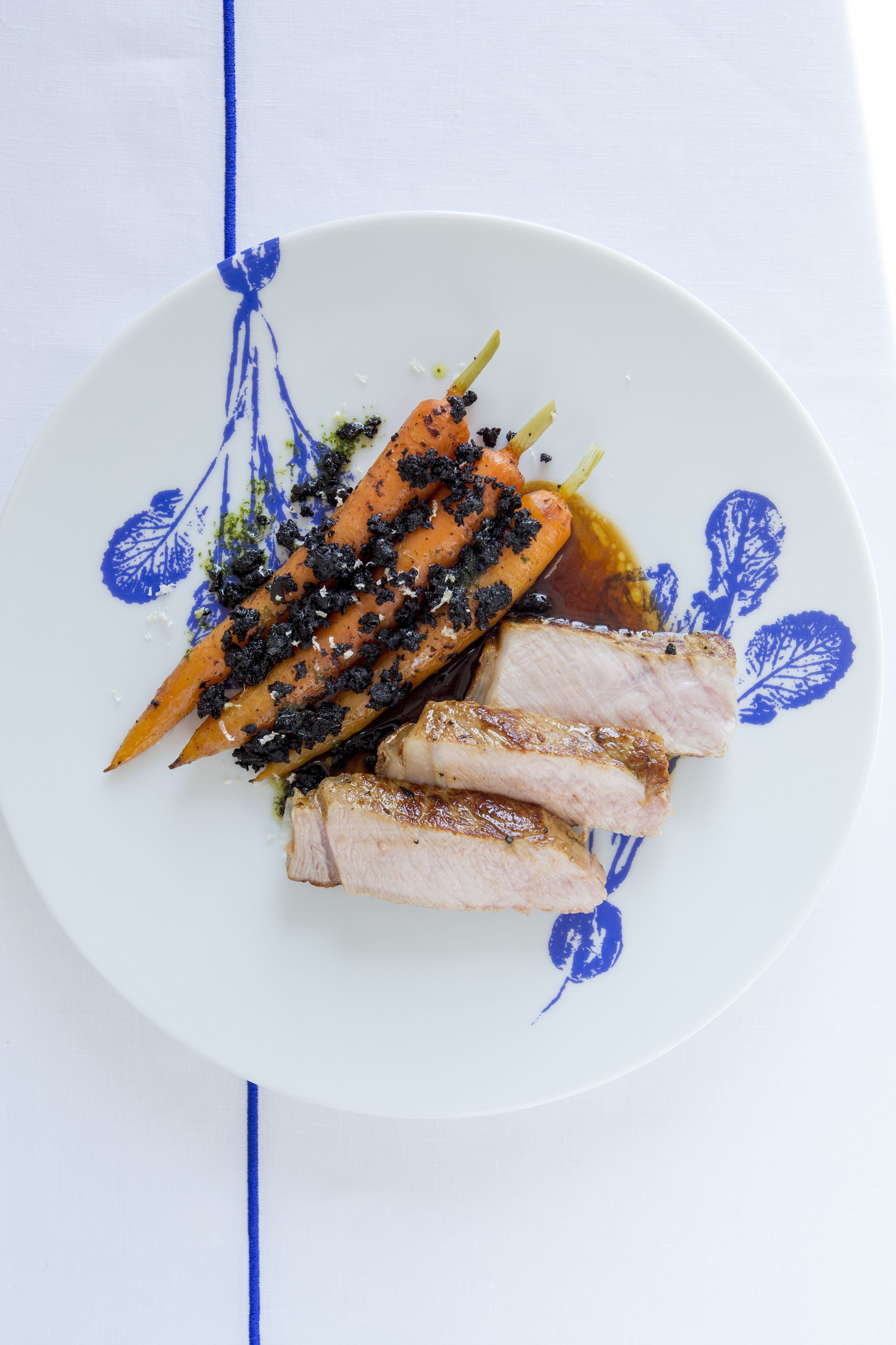 A plate with sliced meat and vegetables, possibly carrots, on a white plate with blue floral patterns.