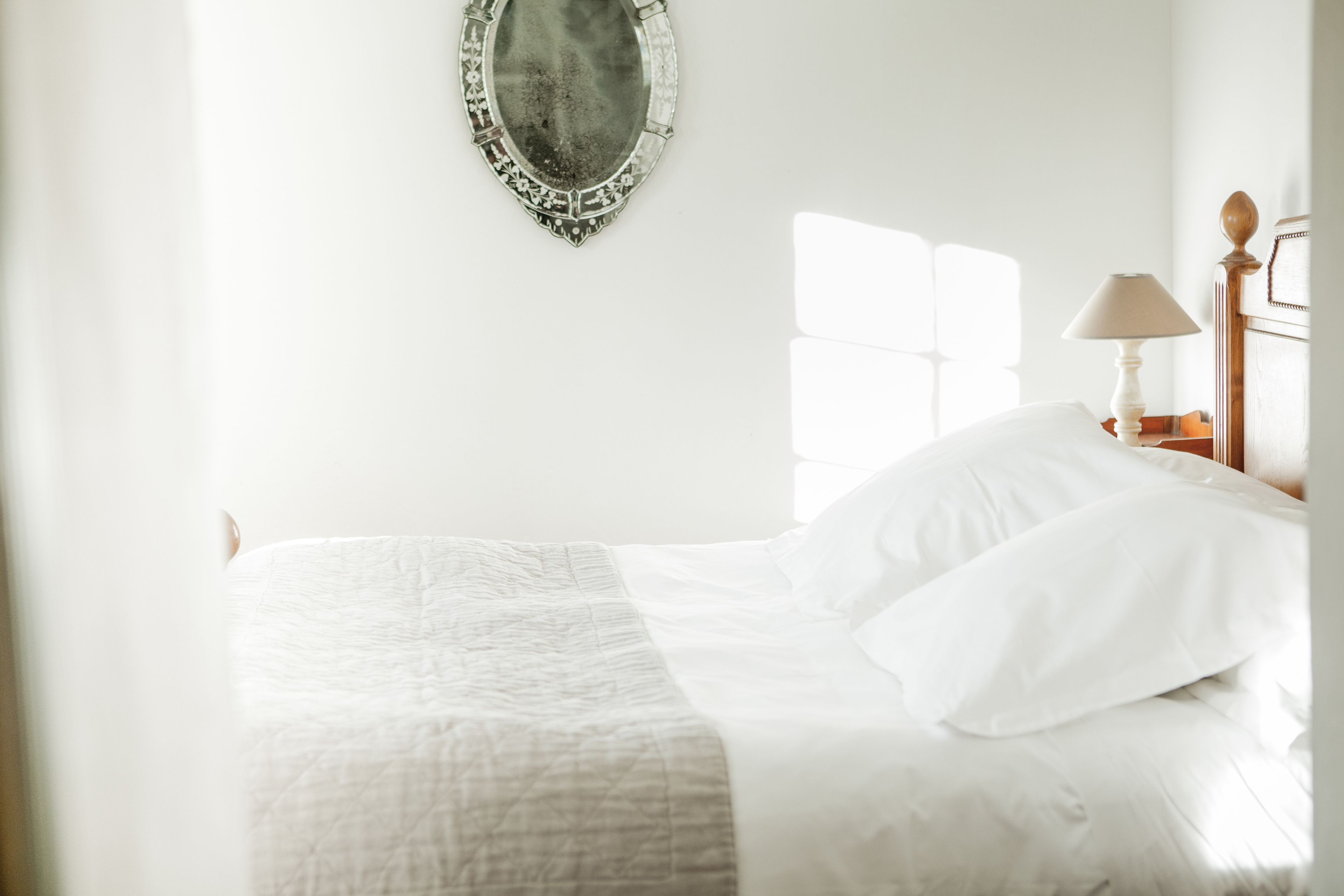 A neatly made bed with white linens, a bedside lamp, and a mirror on the wall.
