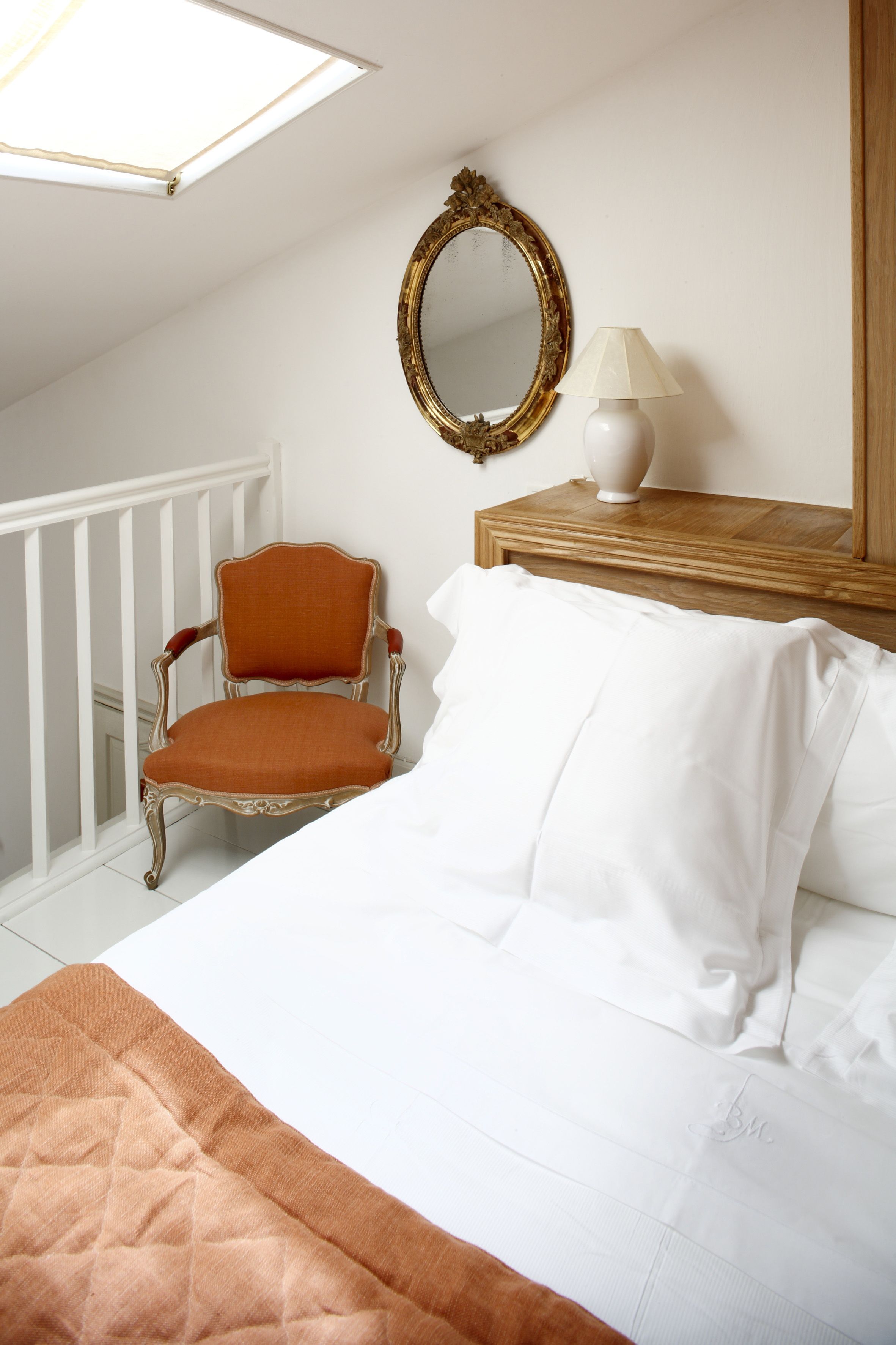 Ein Schlafzimmer mit einem Bett, einem Sessel, einem Spiegel und einer Lampe.