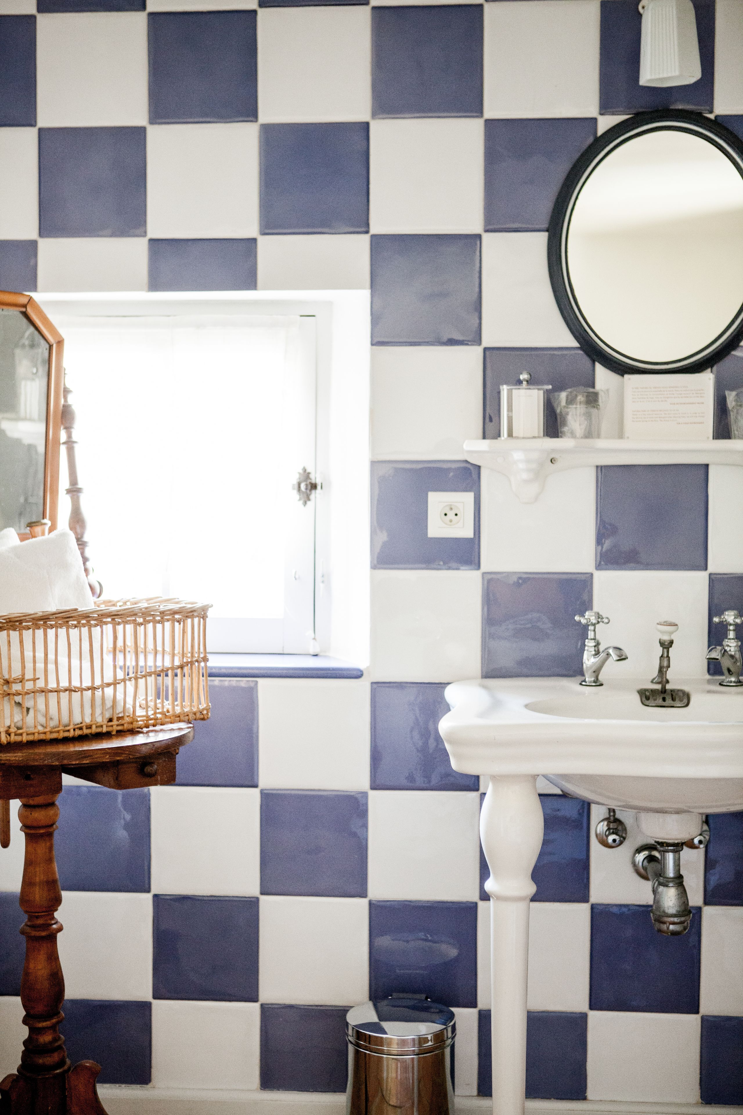 A bathroom with a checkered tile backsplash, a white sink, a wooden chair, and a mirror.