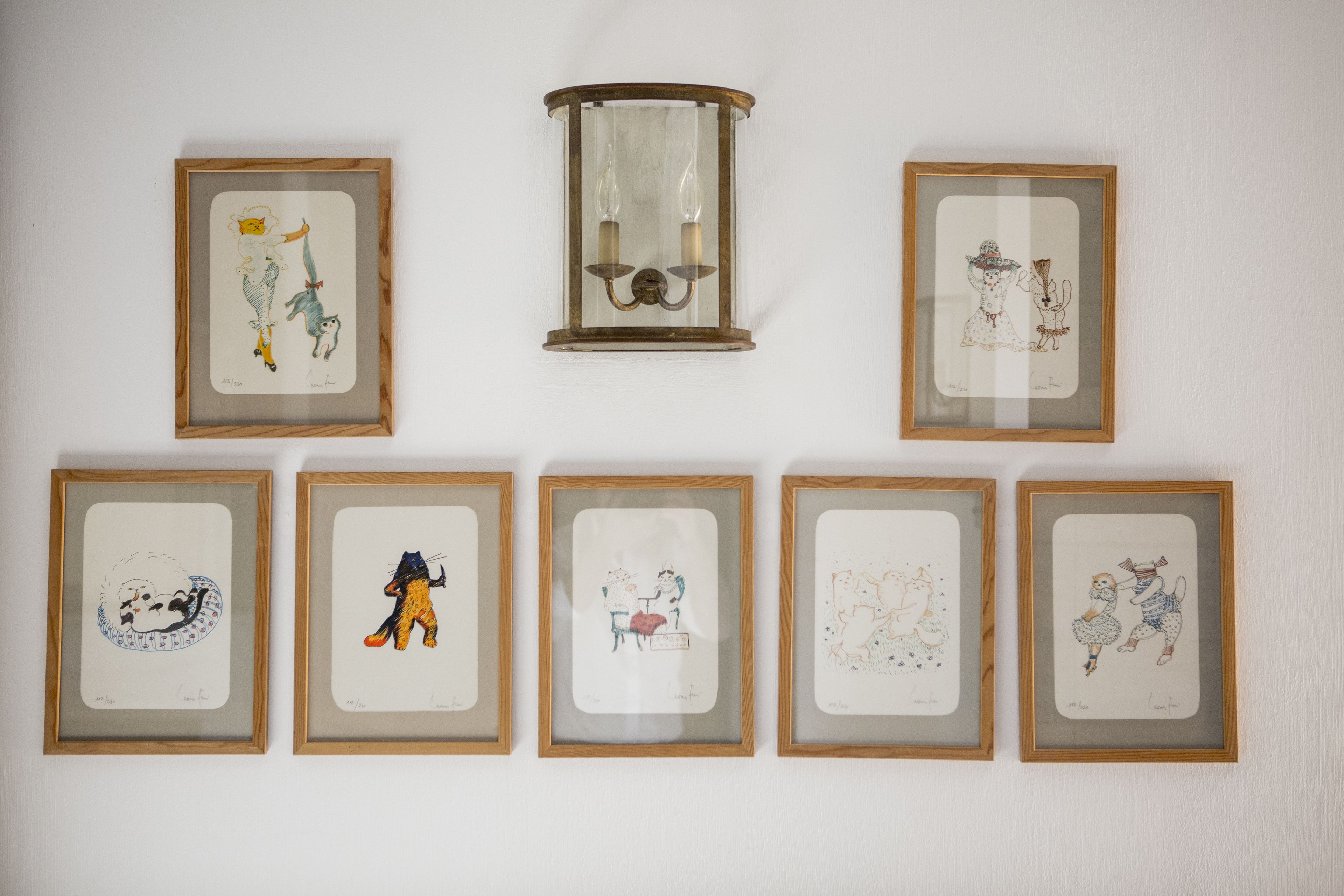 Seven framed artworks on a wall, including a central framed glass artwork with two candles.
