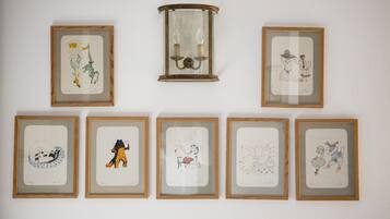 Seven framed artworks on a wall, including a central framed glass artwork with two candles.
