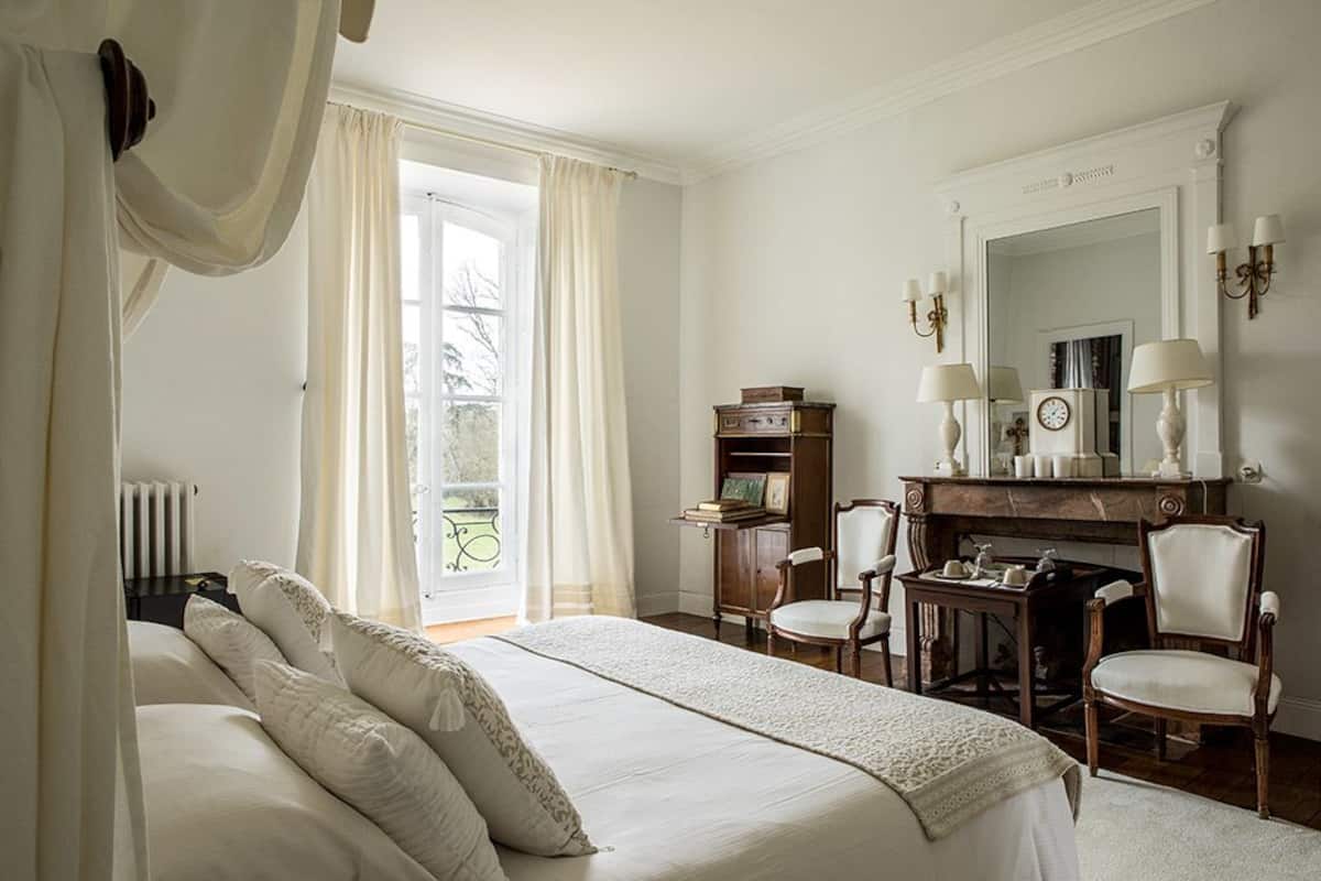 Un dormitorio con una cama grande, un escritorio con silla, una chimenea y un espejo encima.