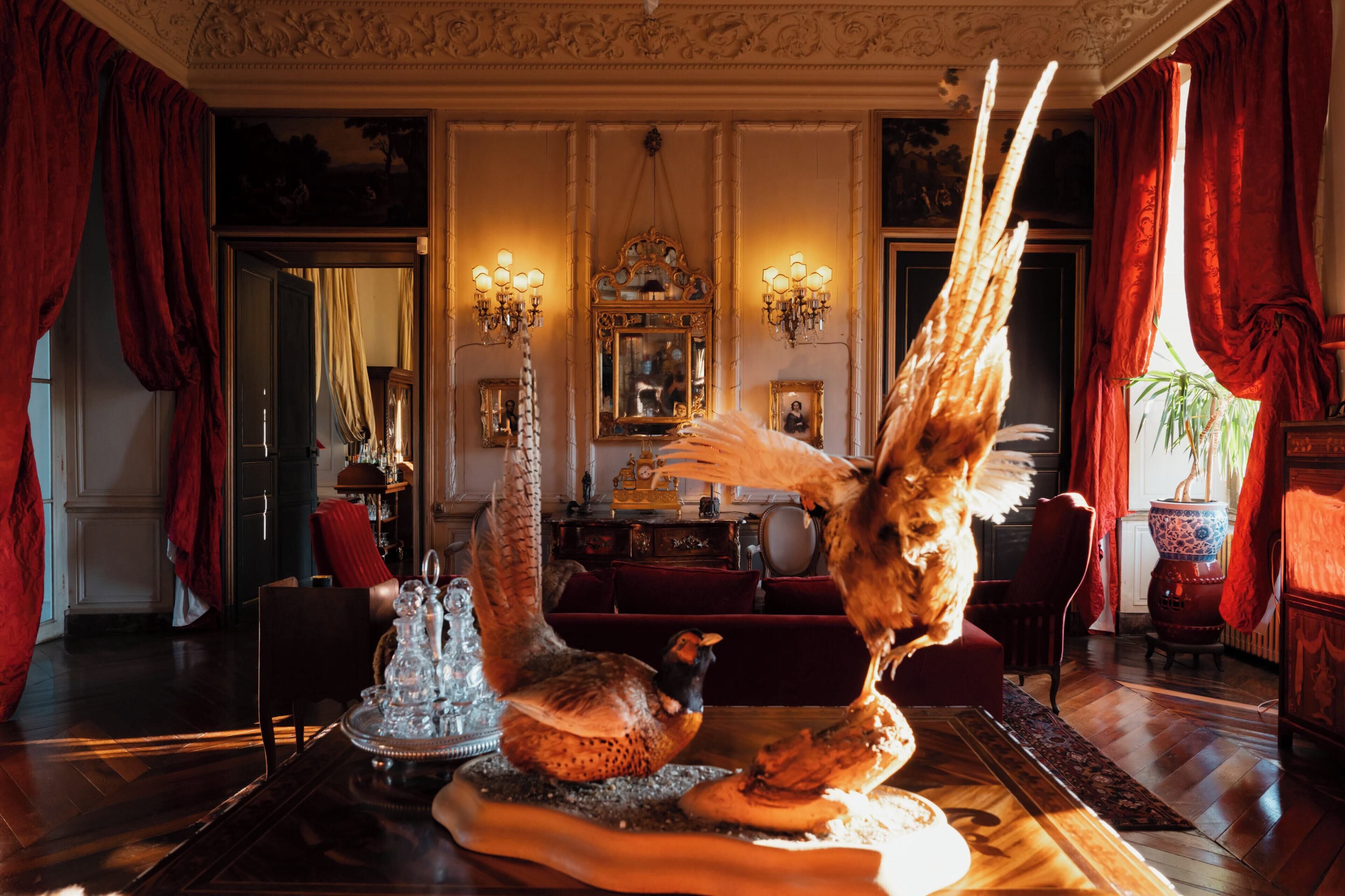 A room with a large bird sculpture, ornate wall decorations, and a chandelier.