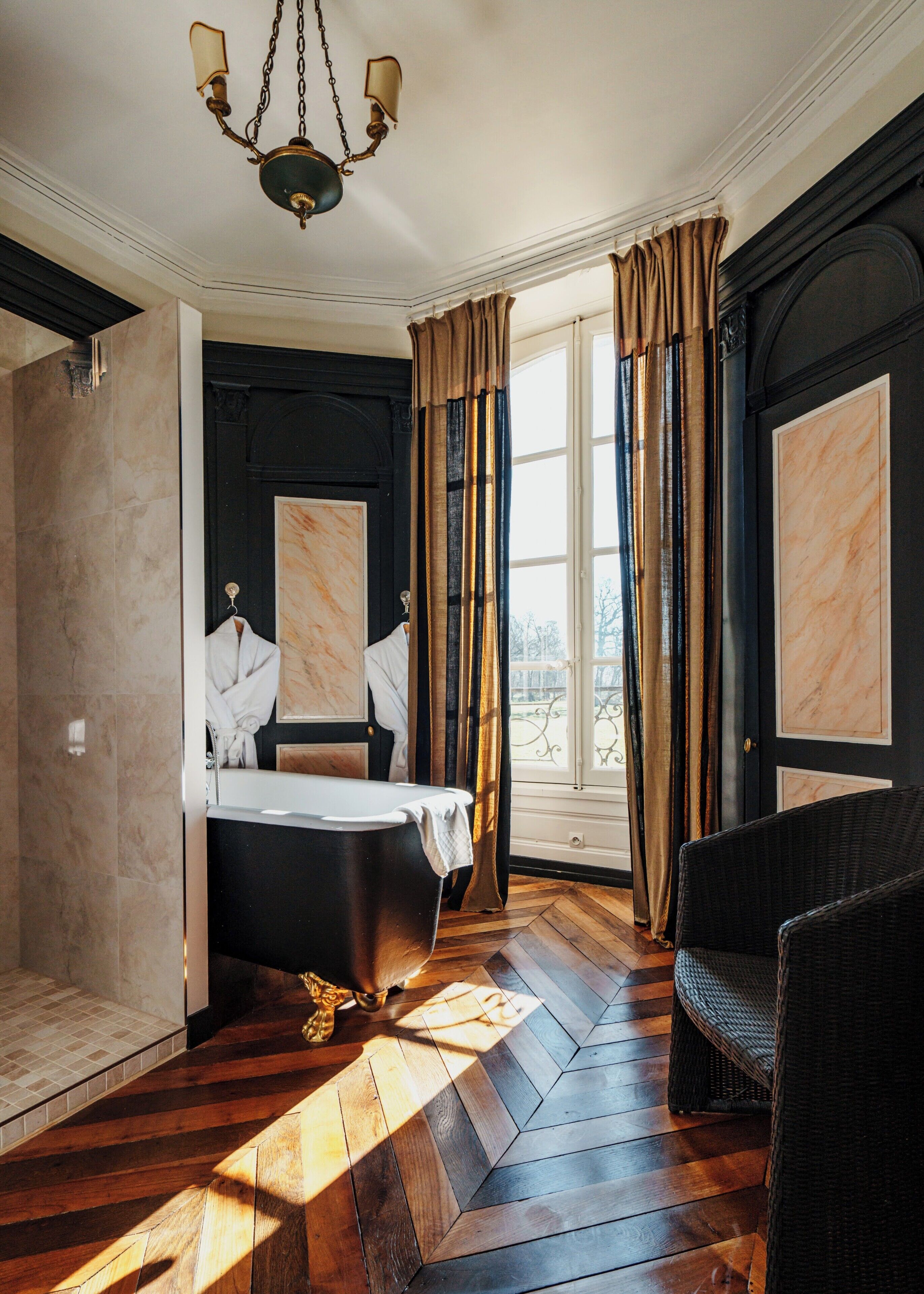 Une chambre avec une baignoire, un fauteuil en osier et une vue sur l’extérieur.