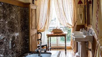 A bathroom with a bathtub, two sinks, and a window with curtains.
