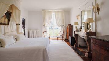 Quarto com uma cama grande, cômoda, cadeira, radiador e vista para o exterior.