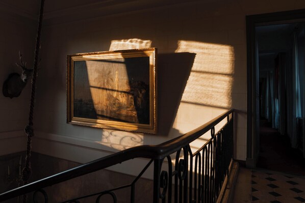 A framed painting on a wall, a staircase with a railing, and a deer head mounted on the wall.