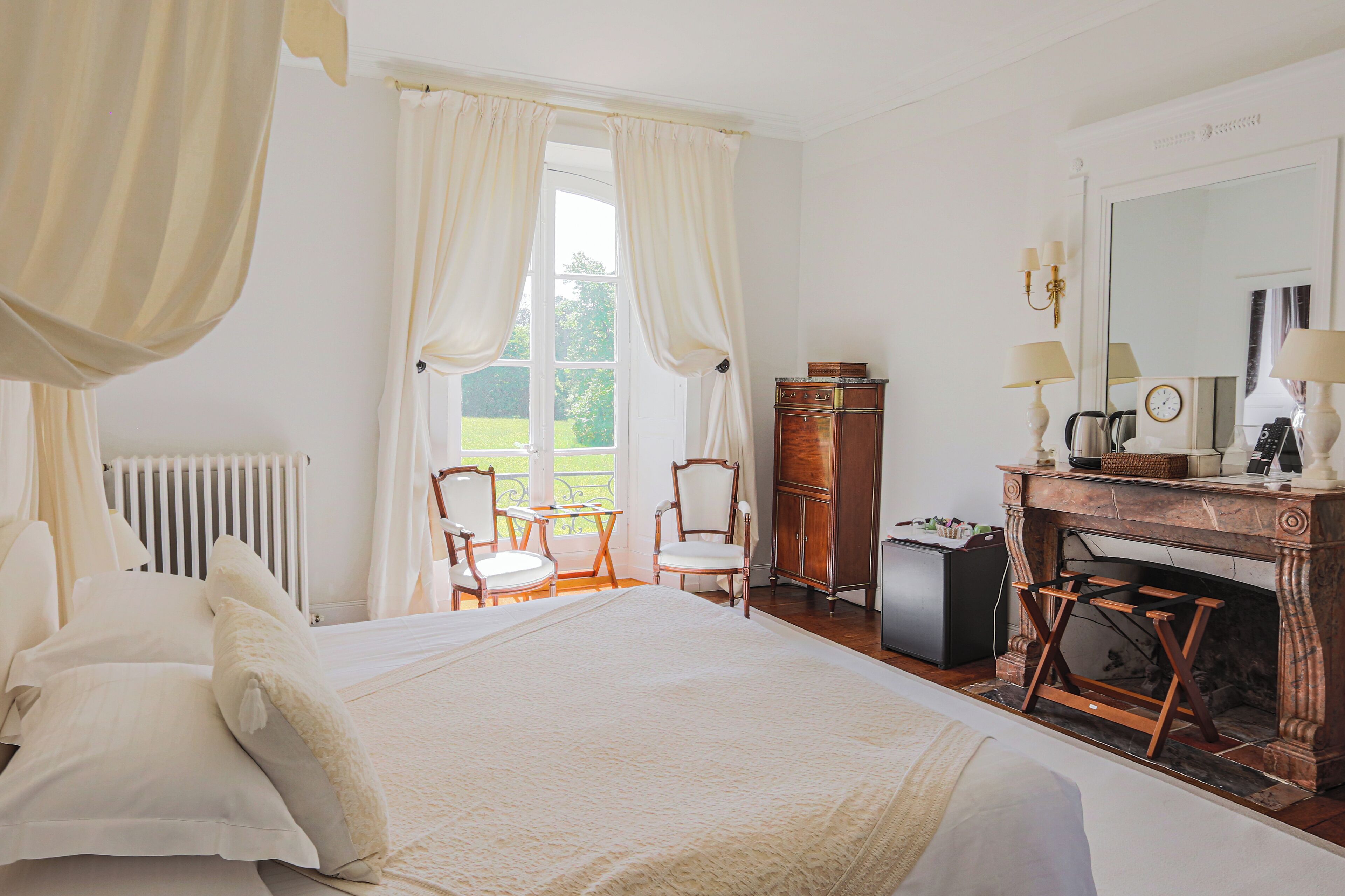 A bedroom with a large bed, a wooden dresser, a fireplace, and a window with curtains.
