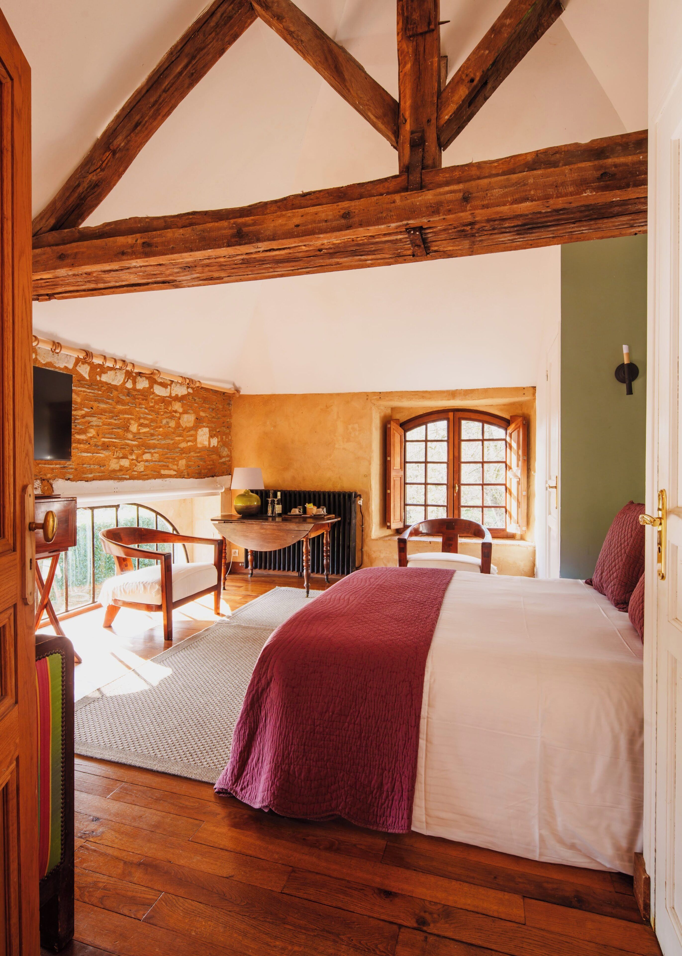 Een kamer met een bed, een tafel, een stoel, een raam en een stenen muur.