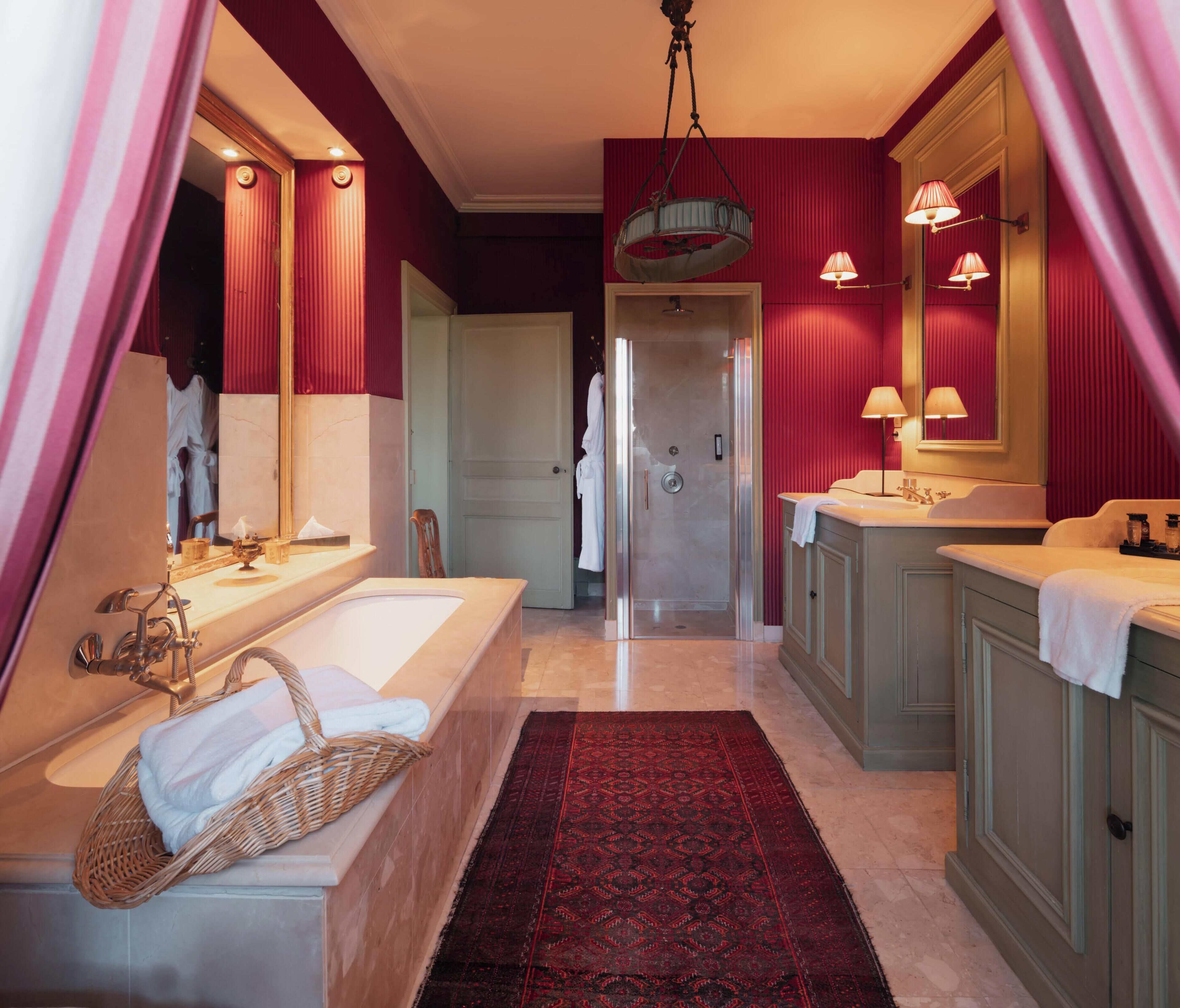 Een badkamer met een bad, een wastafel en een douche. Boven de wastafel hangt een spiegel en aan het plafond een kroonluchter.