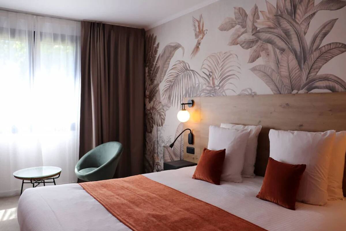 A hotel room with a bed, a nightstand, a lamp, a chair, and a small table.