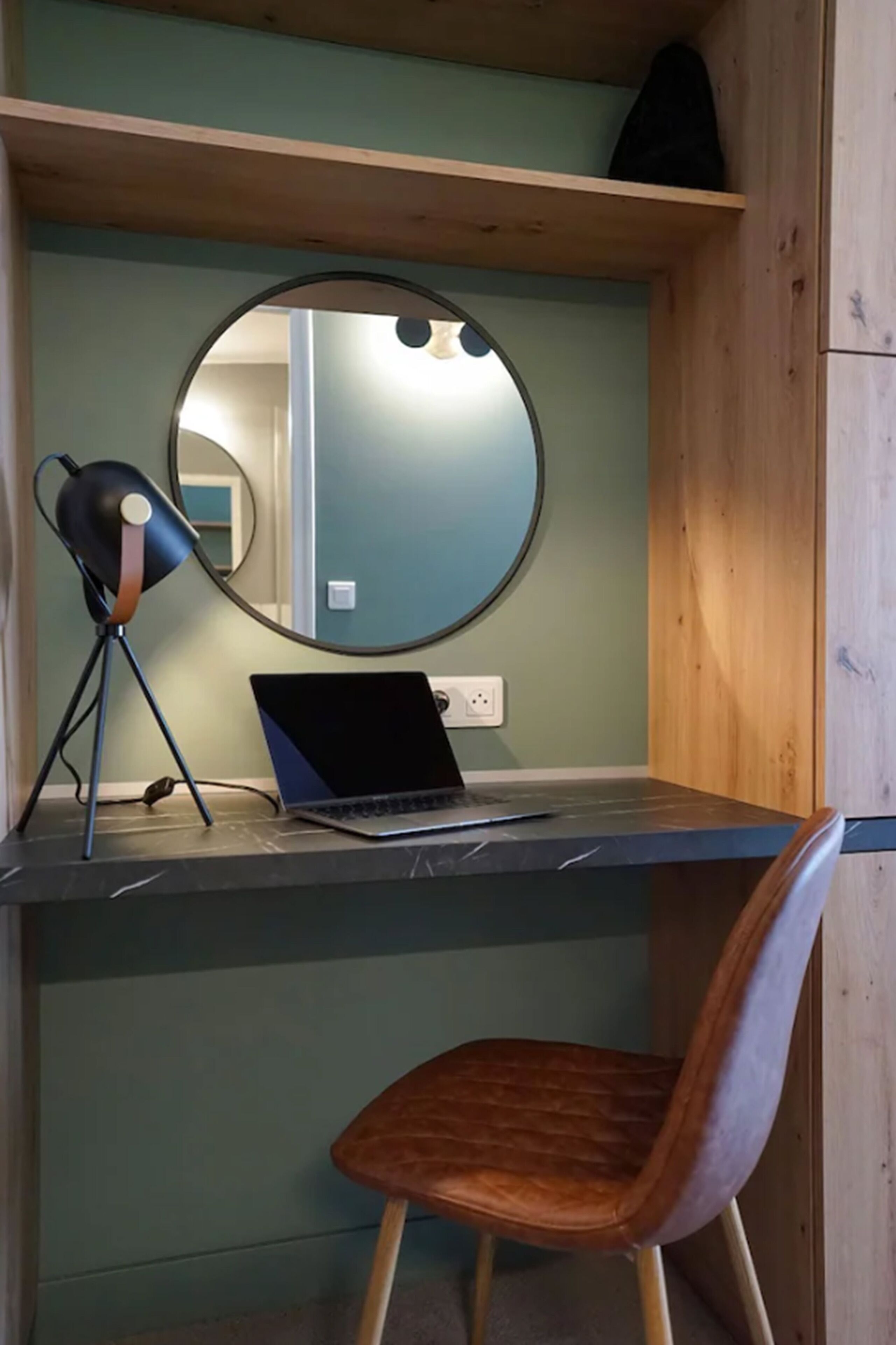 Un espace de travail comprenant un ordinateur portable, une chaise, une lampe et un miroir posé sur une étagère.
