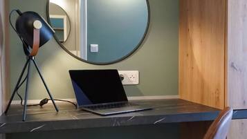 Un espace de travail comprenant un ordinateur portable, une chaise, une lampe et un miroir posé sur une étagère.
